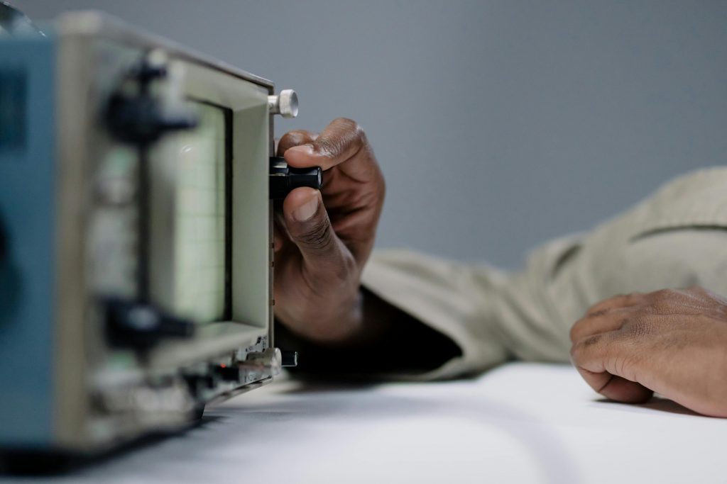 closeup of man's hand turning a dial on an oscilloscope